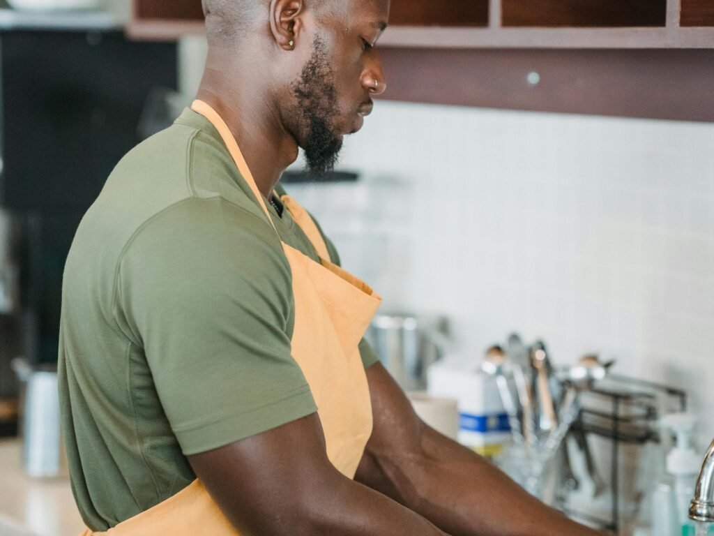 En kjøkkenmedarbeider i forkle står ved oppvasken på et restaurantkjøkken.