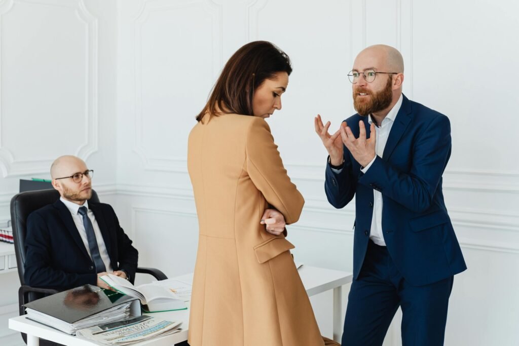 To kolleger i en anspent samtale på et kontor mens en tredje sitter ved pulten.